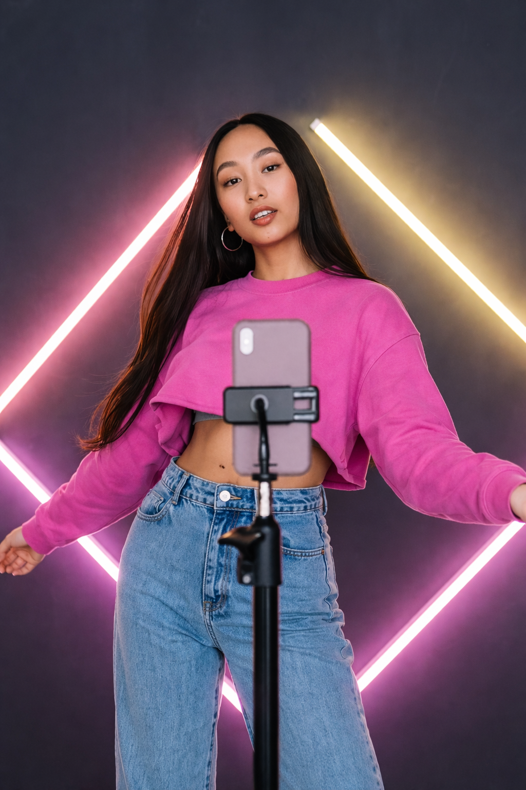Créatrice de contenu Instagram filmant une vidéo avec son smartphone sur trépied, éclairage néon rose et jaune en arrière-plan
